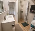 Modern bathroom with a white sink, mirror, glass-enclosed shower, towels, and a Siemens washing machine. The space features wooden flooring and a sleek design.