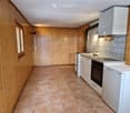 Modern kitchen with wooden walls, tiled floor, white cabinets, sink, oven, and refrigerator.