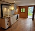 Modern kitchen with white cabinets, stainless steel appliances, tiled floor, and a scenic mountain view through the open door.
