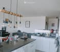 Open-plan living and kitchen area with white cabinets, grey sofa, kitchen island, and modern lighting fixtures.