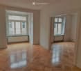 Empty room with wooden flooring, large windows, and radiators. No furniture or equipment present.
