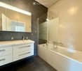 Modern bathroom with a double sink, bathtub, large mirror, and built-in cabinets.