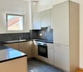 Modern kitchen with light-colored cabinets, stainless steel appliances, and a black countertop. Features a window with a view of a tiled roof.