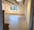 Empty room with exposed wooden beams, tiled floor, large window, and modern lighting fixtures.