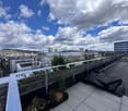 Roof terrace with a metal railing, small planted area, and a rolled-up black mat on the floor.