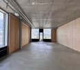 Modern, minimalist corridor with concrete floors and walls, large windows, and exposed wooden paneling.