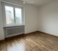 Empty room with wooden flooring, white walls, and a single window with a radiator below it.