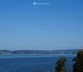 A scenic view of a large lake surrounded by green hills and a town in the distance, with a clear blue sky overhead.