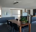 Modern open-plan kitchen and dining area with dark blue cabinetry, a wooden dining table with black chairs, a kitchen island, and a small seating area with a cream-colored armchair.
