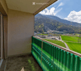 Balcony with green railing, overlooking a scenic valley with mountains, fields, and scattered buildings.