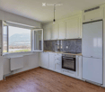 Modern kitchen with white cabinets, wooden flooring, and large windows offering a scenic view. Features include a refrigerator, oven, sink, and faucet.