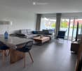 Modern living room with grey sofa, coffee table, dining table, chairs, and a view to a balcony.