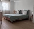 Modern bedroom with a wooden bed, green bedding, two nightstands with lamps, and a window with curtains.
