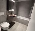 Modern bathroom with grey walls, white toilet, sink, bathtub, and built-in mirrored cabinet.