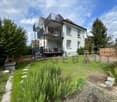 Two-story house with white exterior, dark grey balcony, and well-maintained garden.