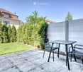 Garden area with a patio, a small table, and two chairs, surrounded by greenery and a fence.