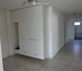 Empty hallway with tiled floor, white walls, built-in white closet with drawers and shelves, and a small window at the end.