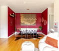 Modern living room with red accent walls, white sofa, dining table with chairs, and decorative elements including a large artwork and plants.