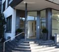 Modern building entrance with concrete steps, glass doors, and potted plants on either side.