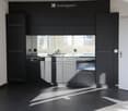Modern kitchen with dark grey cabinets, stainless steel appliances, and a black tiled floor. Features a sink, faucet, dishwasher, and oven.