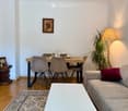 A modern living and dining area with a sofa, coffee table, dining table, chairs, a floor lamp, a plant, and a decorative clock on a side table.