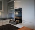 kitchen with a stainless steel oven, granite counter, white cabinets, glass display cabinet, granite slab, and tiled floor