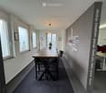 Dining room, large wooden table, chairs, carpet, wall with hanging clothes, windows, wall with writings