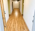 A long, narrow hallway with wooden flooring and white walls, featuring several doors on both sides and exposed wooden beams on the ceiling.
