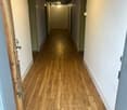 A long, narrow hallway with wooden flooring, white walls, and green doors on both sides.