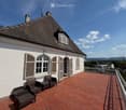 Balcony with brick tiles, metal railing, and several wicker chairs and a small table.