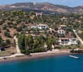 Aerial view of a coastal village with houses, trees, and a beach, surrounded by hills and mountains.