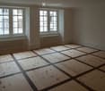 Empty room with wooden floor and large windows, featuring radiators under the windows.