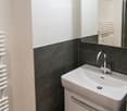 Modern bathroom with a white sink, chrome faucet, dark tiled walls, and a white radiator.