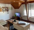 A furnished attic room with wooden floor, wooden ceiling, large windows, sofa, coffee table, and television