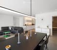 Modern open-plan living and dining area with a black leather sofa, coffee table, dining table with chairs, and a small kitchen area with cabinets and a sink.
