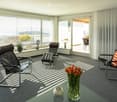 modern living room with large windows, black leather chairs, glass table, flowers, balcony