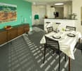 Dining room with a table, chairs, and a green wall with a painting. A counter with stools and a refrigerator is visible in the background.