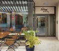 Outdoor seating area with wooden tables and chairs, a potted plant, and a storefront with a sign reading "Stay Sunday".