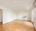 Completely empty room with white walls, wooden floor, and a small built-in desk area with a mirror. No furniture or equipment.