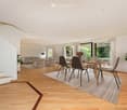 Open-plan living and dining area with wooden flooring, modern furniture, large windows, and a staircase leading to an upper level.