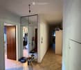 A narrow hallway with tiled flooring, a decorative mosaic rug, and a mirrored closet. The hallway leads to a bathroom and other rooms, with a light fixture hanging from the ceiling.