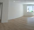Empty room with light wooden flooring, white walls, and a large window with an open door leading to another space.