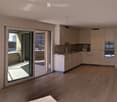 Modern kitchen with light-colored cabinets, a stove, an oven, and a sink, connected to a spacious living area with wooden flooring and large glass doors leading to a balcony.