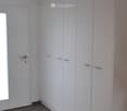 Empty room with white built-in wardrobes, wooden flooring, and a small window near the door.
