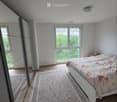 Bright bedroom with wooden flooring, large window, bed with floral bedding, and patterned rug.