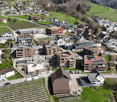 Aerial view of a residential area with multiple houses, apartment buildings, and green spaces. Some buildings have solar panels on their roofs, and there are construction cranes visible in the area.
