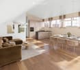 Open-plan living and dining area with a brown sectional sofa, coffee table, dining table with chairs, kitchen island, and pendant lights.