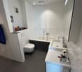 Modern bathroom with white tiles, a bathtub, a sink, a toilet, and a mirror. The sink has a cup and toothbrush on it, and there is a towel hanging on the side.