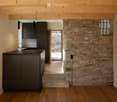 modern kitchen with black cabinets, wooden floor, stone wall, open door leading to outdoor area