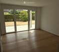 Empty room with wooden flooring and large sliding glass doors leading to a patio area with a view of a garden.